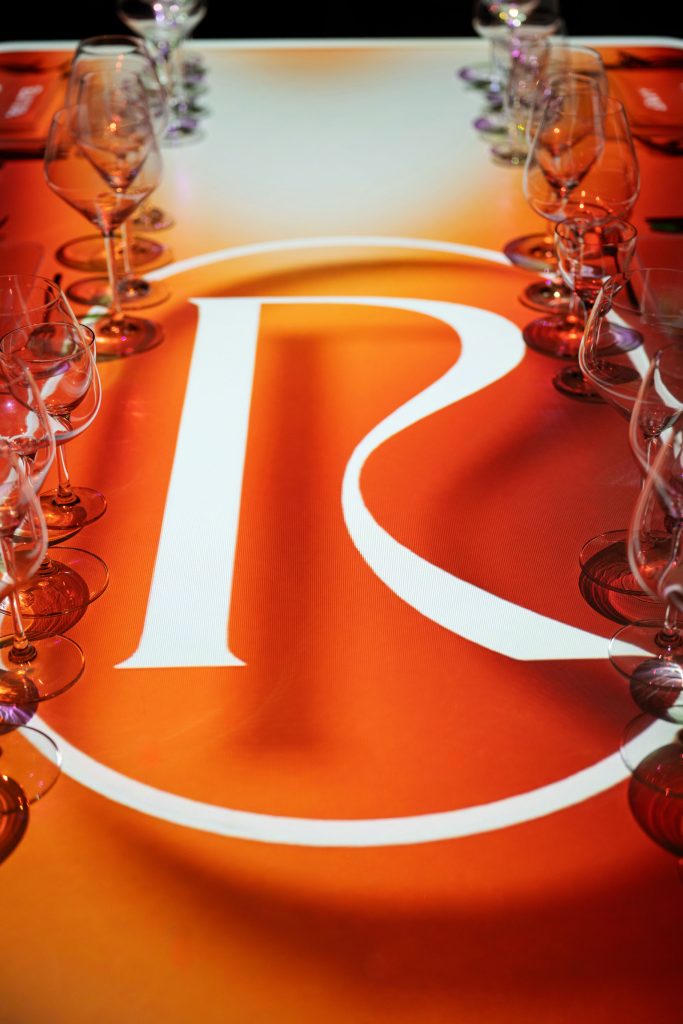 The Radiant Table with bold orange projection featuring a large stylized “R” centerpiece design