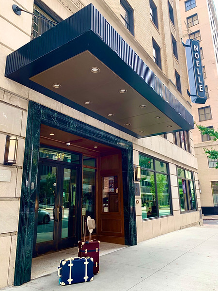 Noelle Nashville hotel entrance with stylish luggage on sidewalk and bold vertical hotel sign.
