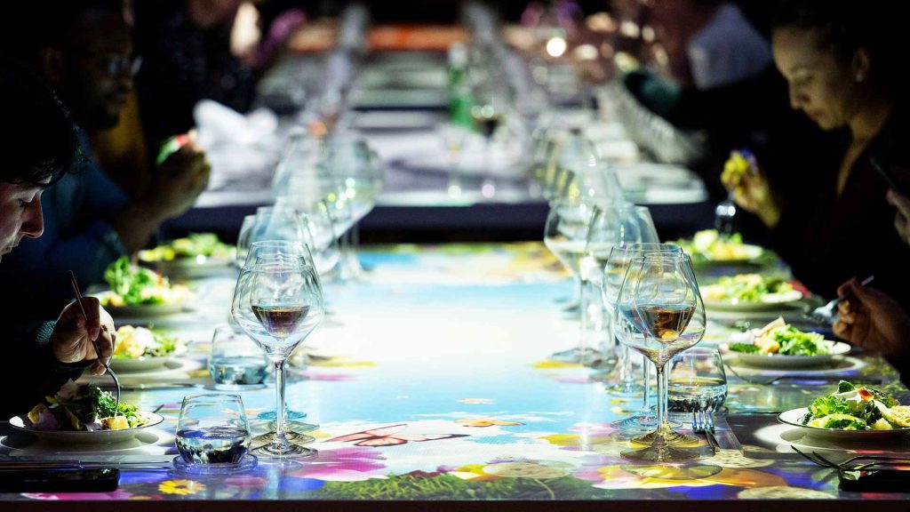 Guests dining at The Radiant Table with vibrant floral and butterfly-themed projection display