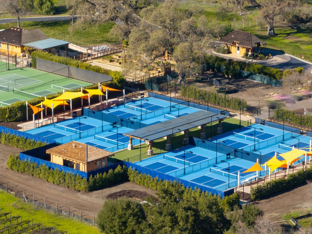 Aerial view of CordeValle’s tennis and pickleball complex featuring bright blue courts and shaded seating areas.