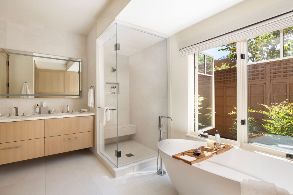 Bright spa-like bathroom at CordeValle with walk-in glass shower, double vanity, and freestanding tub facing a private garden.