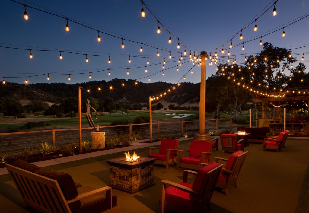 Cozy outdoor firepit lounge at CordeValle with string lights and scenic golf course backdrop for evening relaxation.