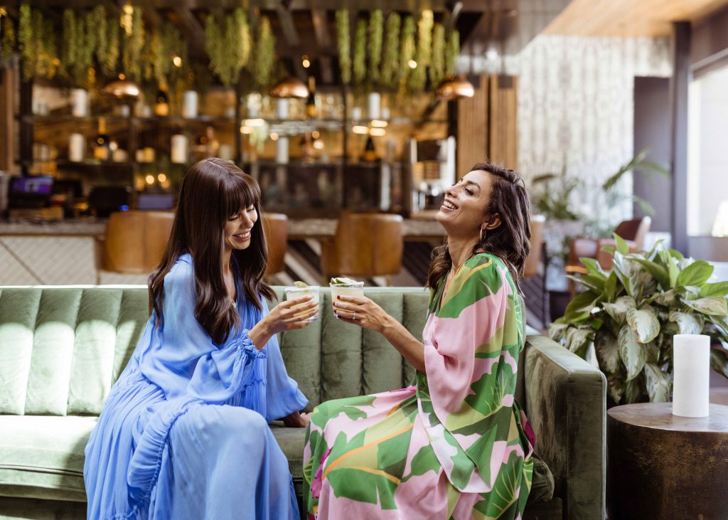 Two women enjoying cocktails and laughing at a stylish Scottsdale lounge