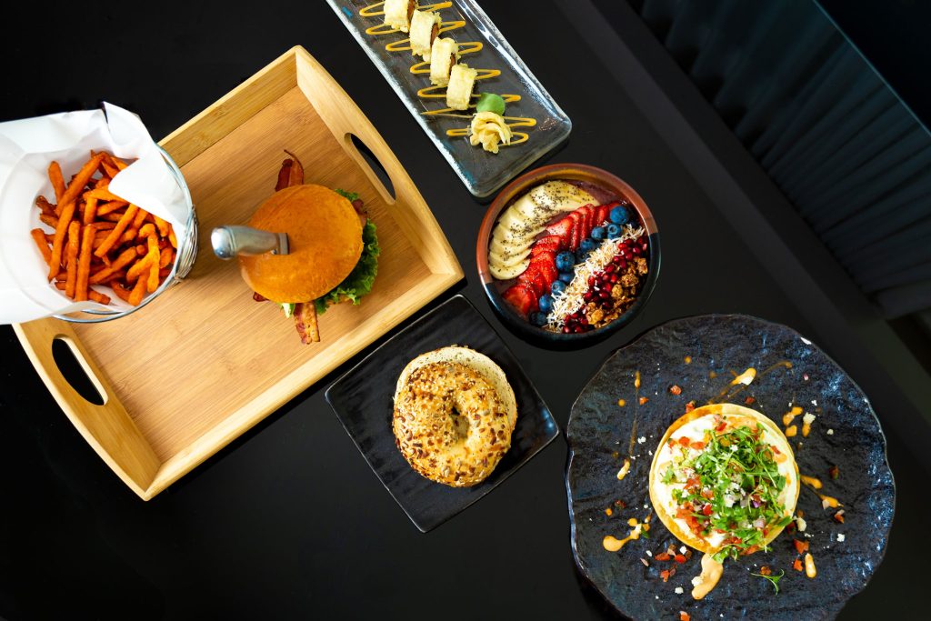 Gourmet hotel dining spread with burger, fries, sushi, and smoothie bowl
